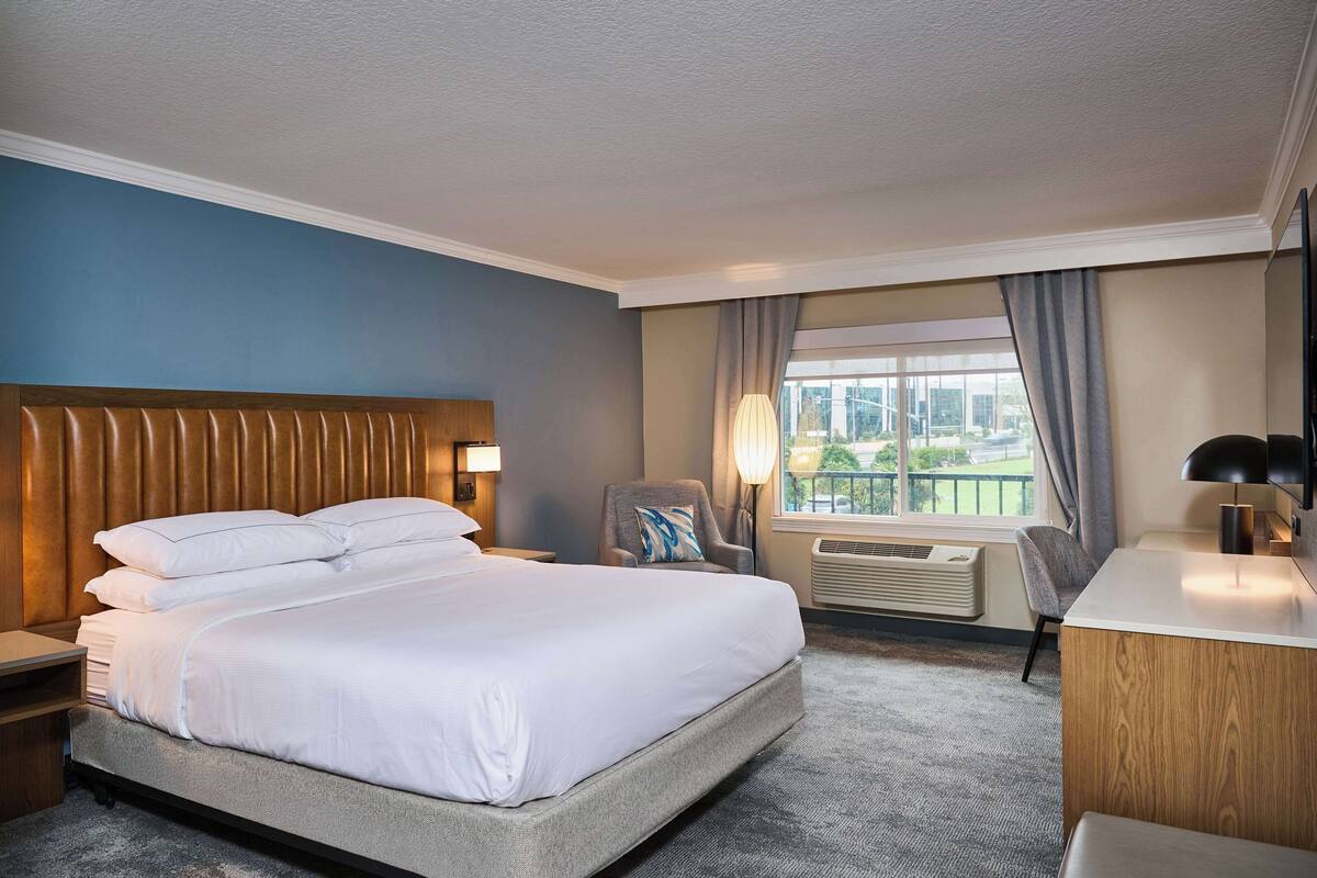 A hotel room with a large bed, a desk, a chair, and a window with a view.