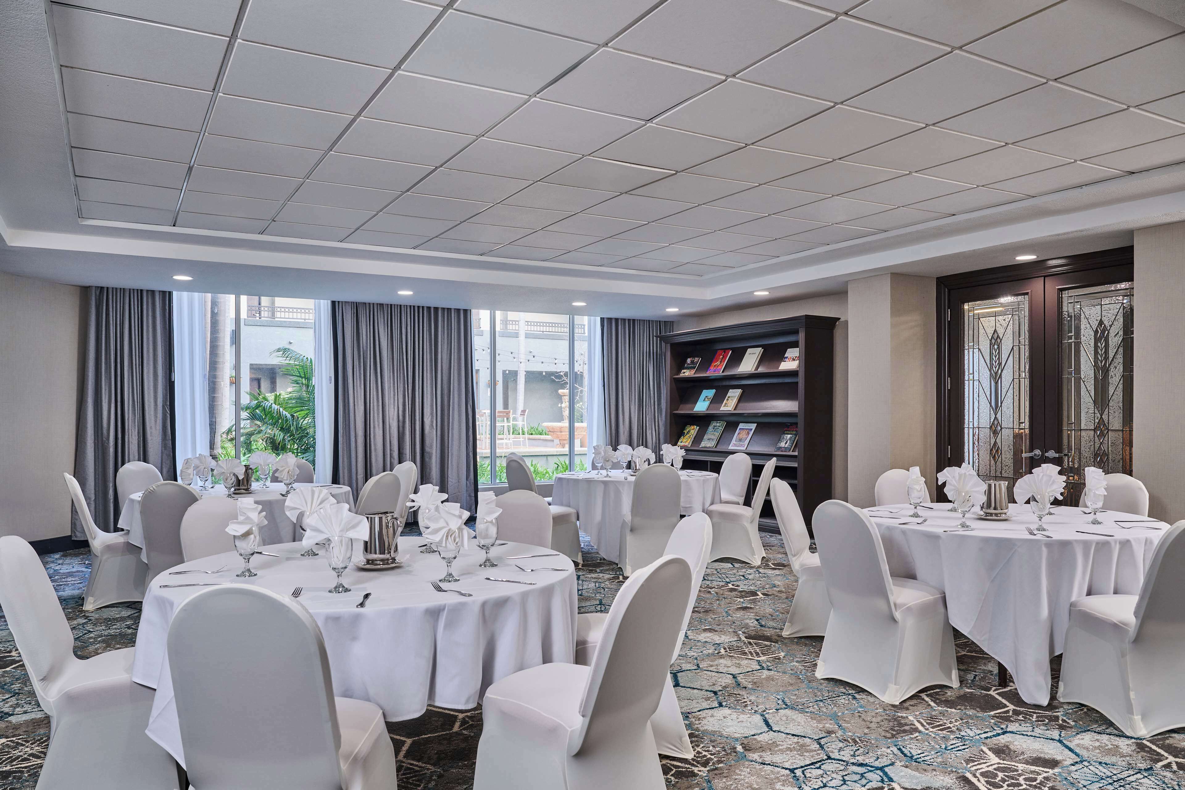 Une salle de conférence avec plusieurs tables rondes, des chaises blanches et une bibliothèque.