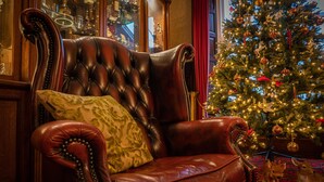 A leather armchair with a patterned pillow, positioned near a Christmas tree adorned with ornaments and lights. - Ledgowan Lodge Hotel (Achnasheen)