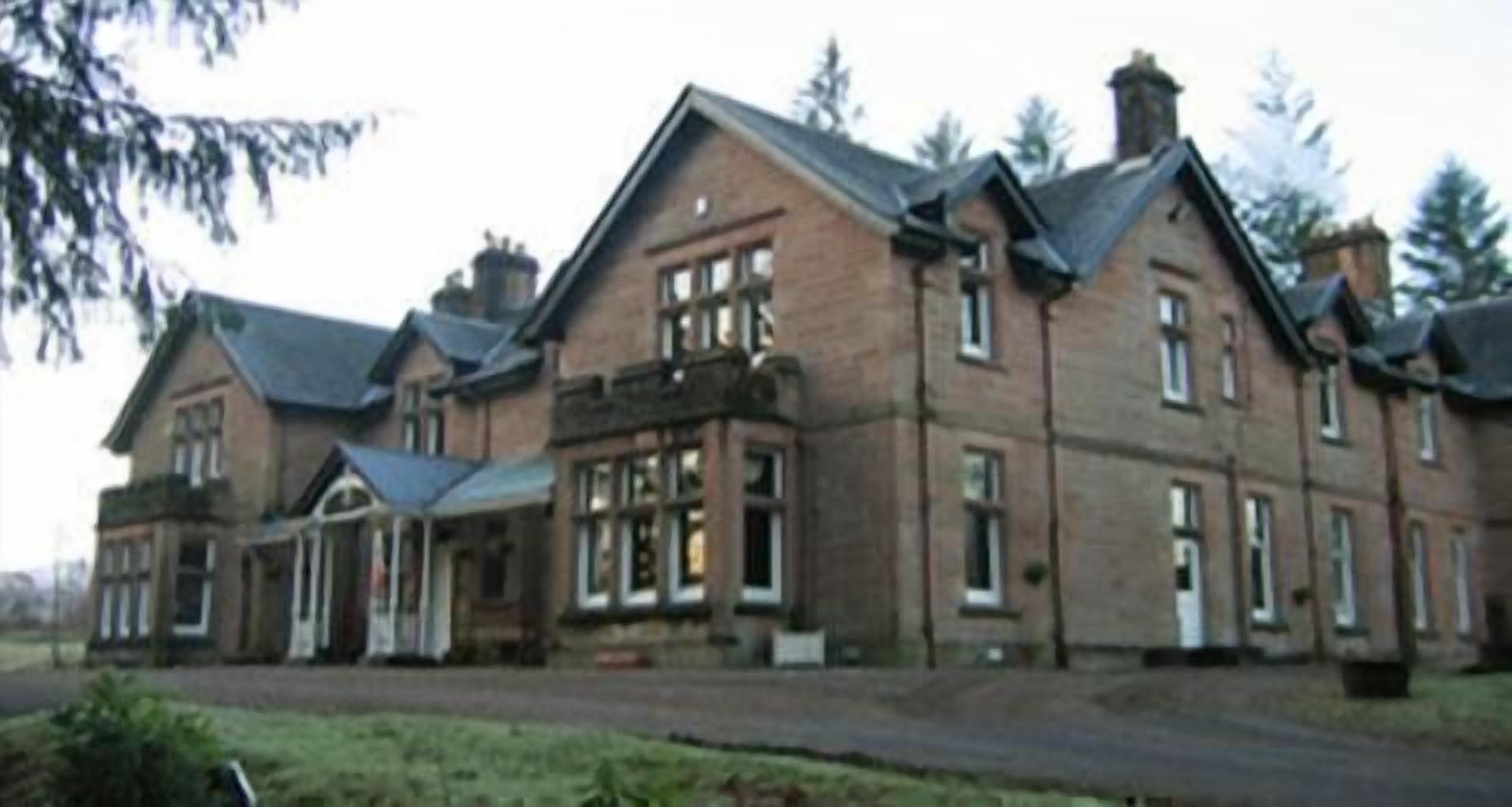A large, multi-story building with a symmetrical facade, featuring a central entrance with a covered porch and multiple windows.