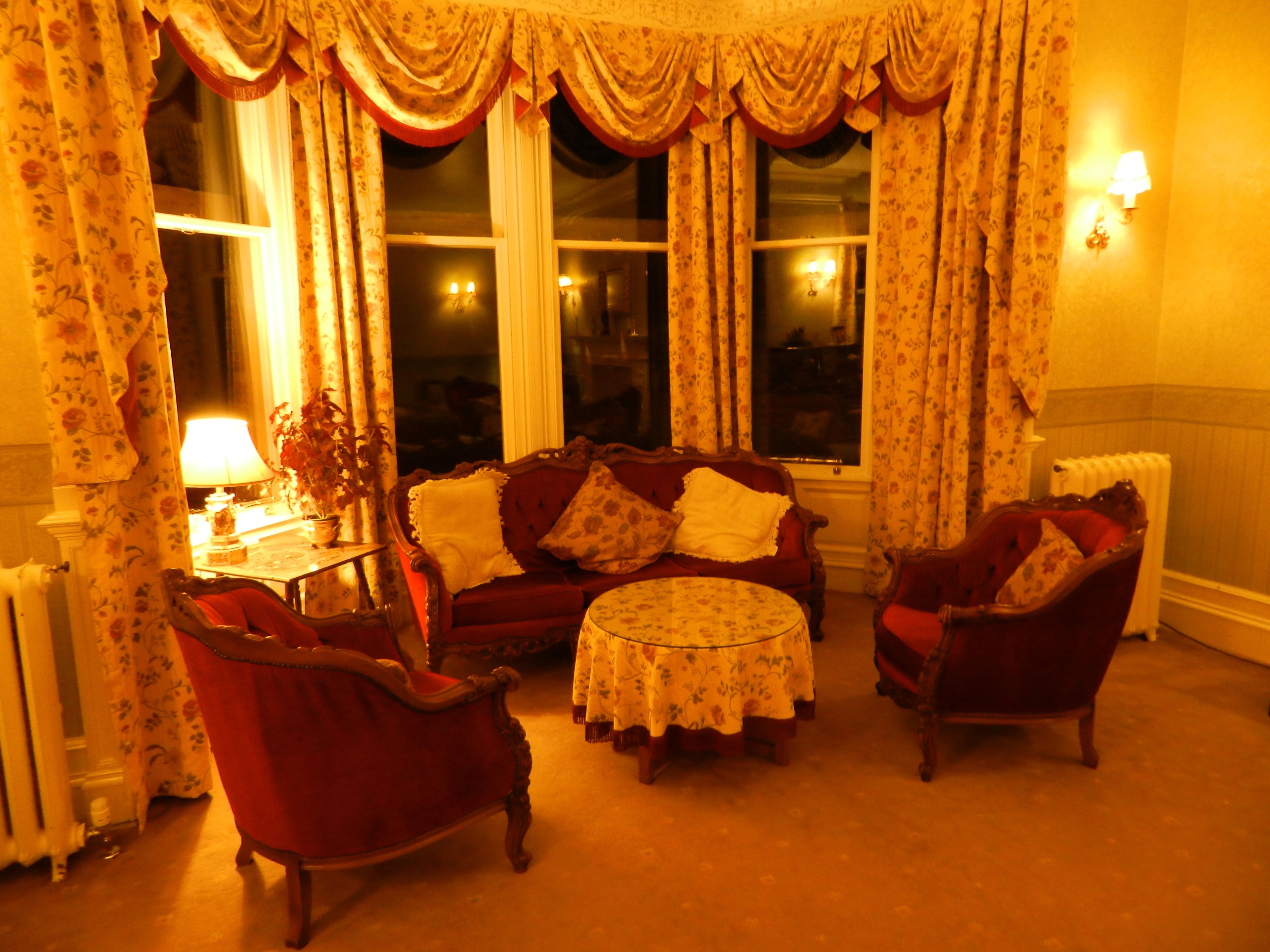 A cozy living room with a red sofa, two armchairs, a round coffee table, and floral curtains.