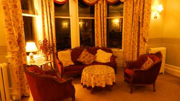 A cozy living room with a red sofa, two armchairs, a round coffee table, and floral curtains.
