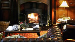 A cozy room with a fireplace, leather sofa, and a table set with tea service. - Ledgowan Lodge Hotel (Achnasheen)