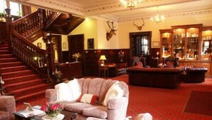 A grand lobby with a red carpet, a staircase, plush seating, and a mounted deer head. - Ledgowan Lodge Hotel (Achnasheen)