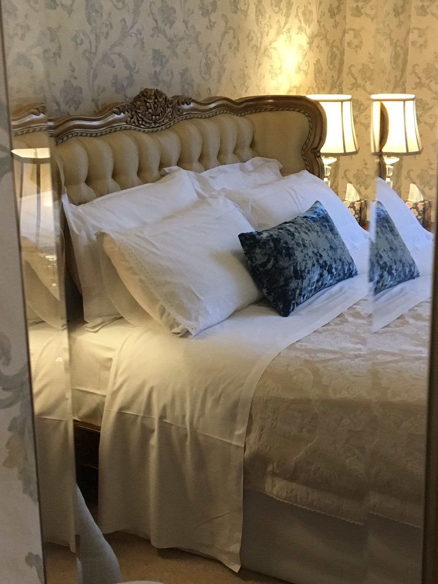 Un lit doté d’une tête de lit capitonnée, de draps blancs et de deux oreillers, dont l’un est orné d’un motif bleu.