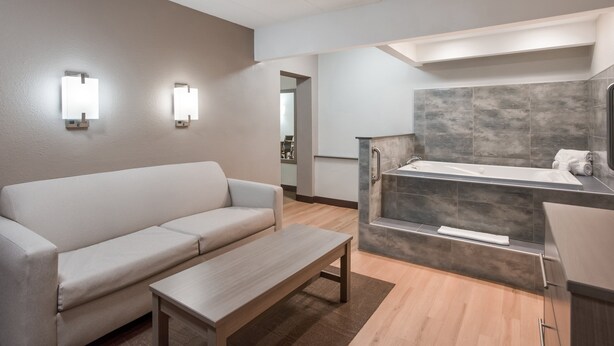 Ein modernes Hotelzimmer mit einer Sitzecke, einem Holztisch, einer Badewanne und zwei Wandleuchten.