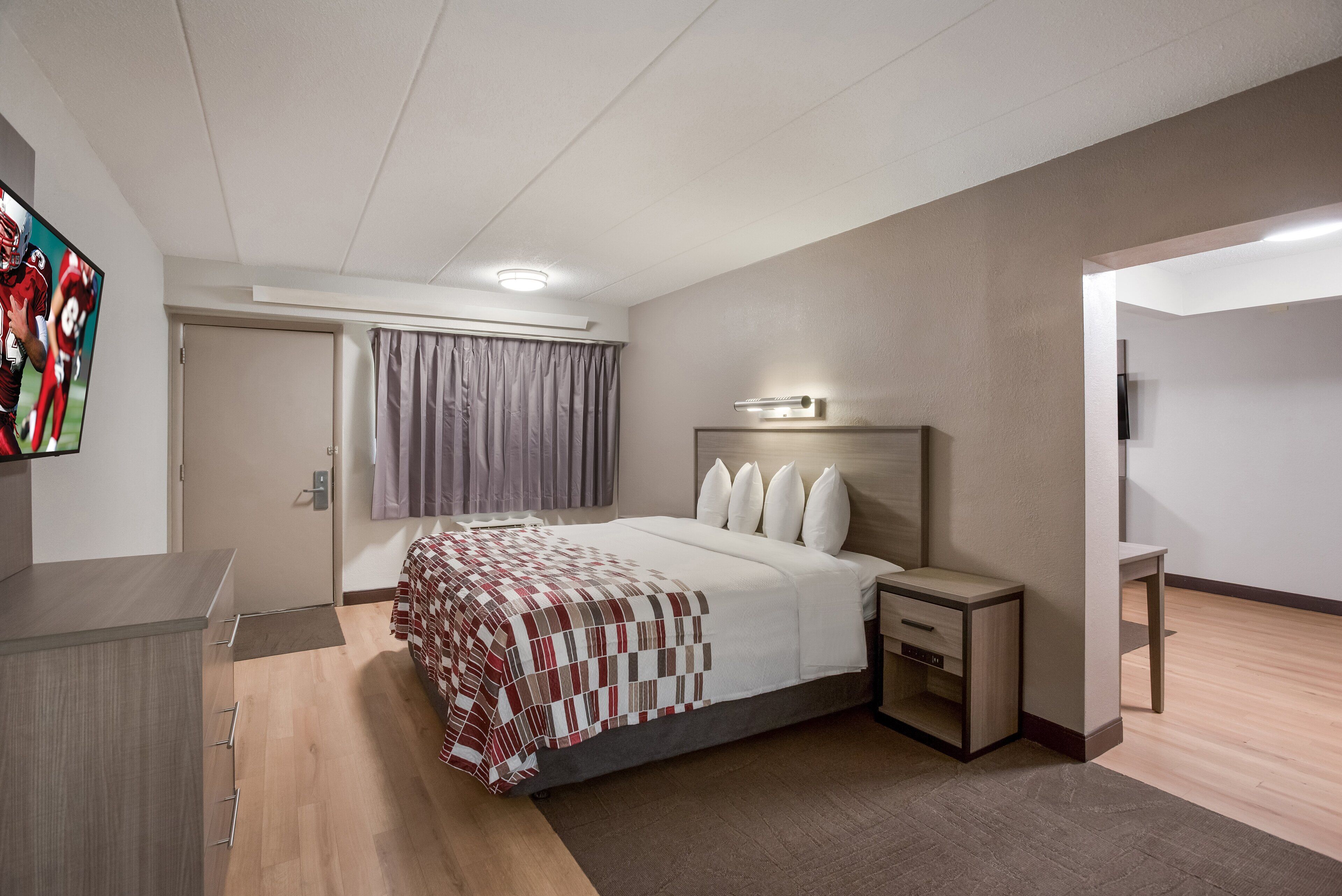 Une chambre d’hôtel moderne, dotée d’un grand lit, d’une table de chevet et d’un téléviseur à écran plat fixé au mur.