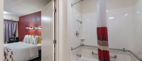 Habitación de hotel con cama, ducha con barra de seguridad y baño con bañera.