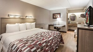 Ein Hotelzimmer mit einem großen Bett, einem Schreibtisch, einem Sessel, einem Fernseher und einem Badezimmer mit Spiegel und Waschbecken.
