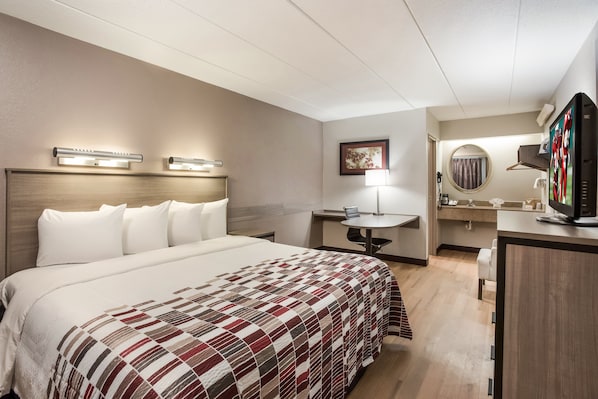 A hotel room with a large bed, a desk, a chair, a television, and a bathroom with a mirror and sink.