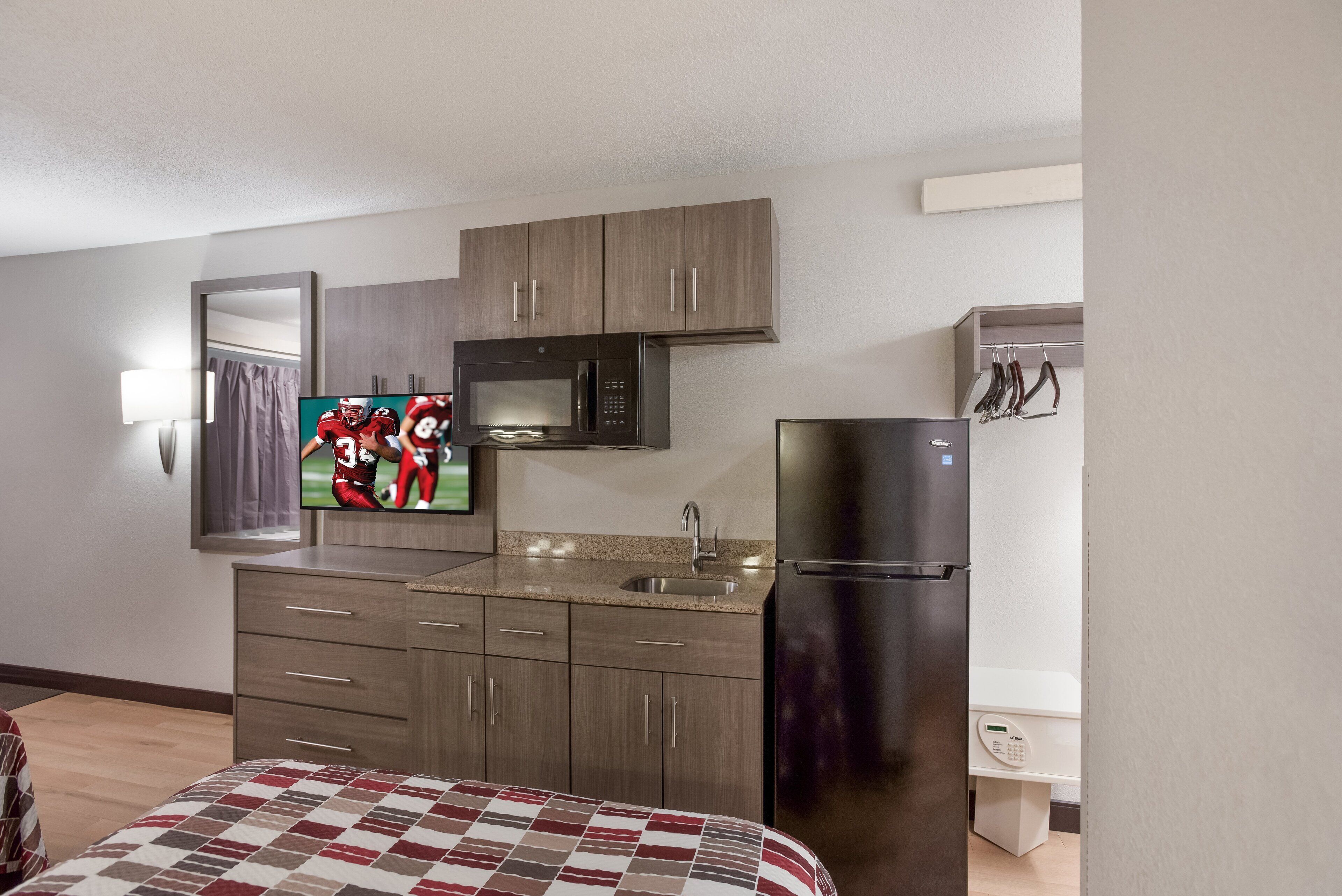 Una habitación de hotel compacta con kitchenette, que incluye microondas, refrigerador y pileta.