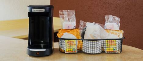 A coffee maker and a basket of packaged food items on a countertop.
