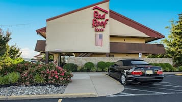 A Red Roof Inn building with a beige facade, a red roof, and an American flag.