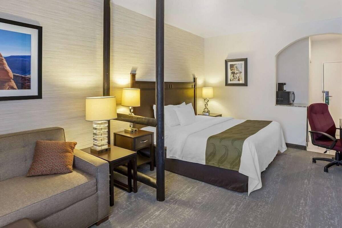Una habitación de hotel con cama, mesitas de noche, escritorio, silla, sofá y un cuadro en la pared.