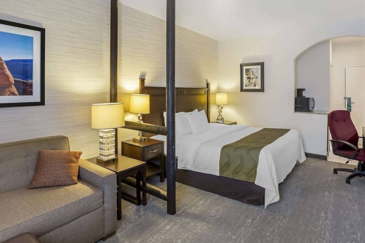 A hotel room with a bed, bedside tables, a desk, a chair, a couch, and a framed picture on the wall.
