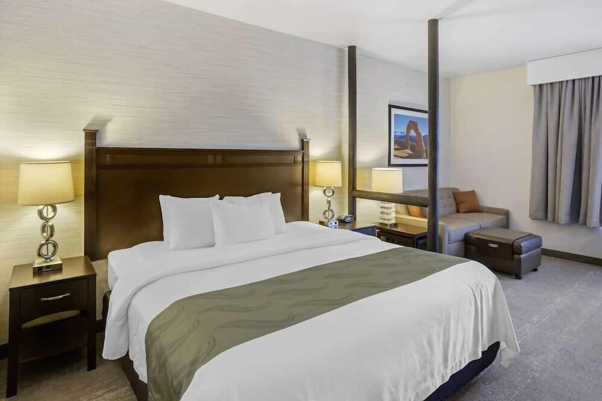 Quarto de hotel com uma cama grande, duas mesas de cabeceira com luminárias, um sofá, uma mesinha e um quadro na parede.