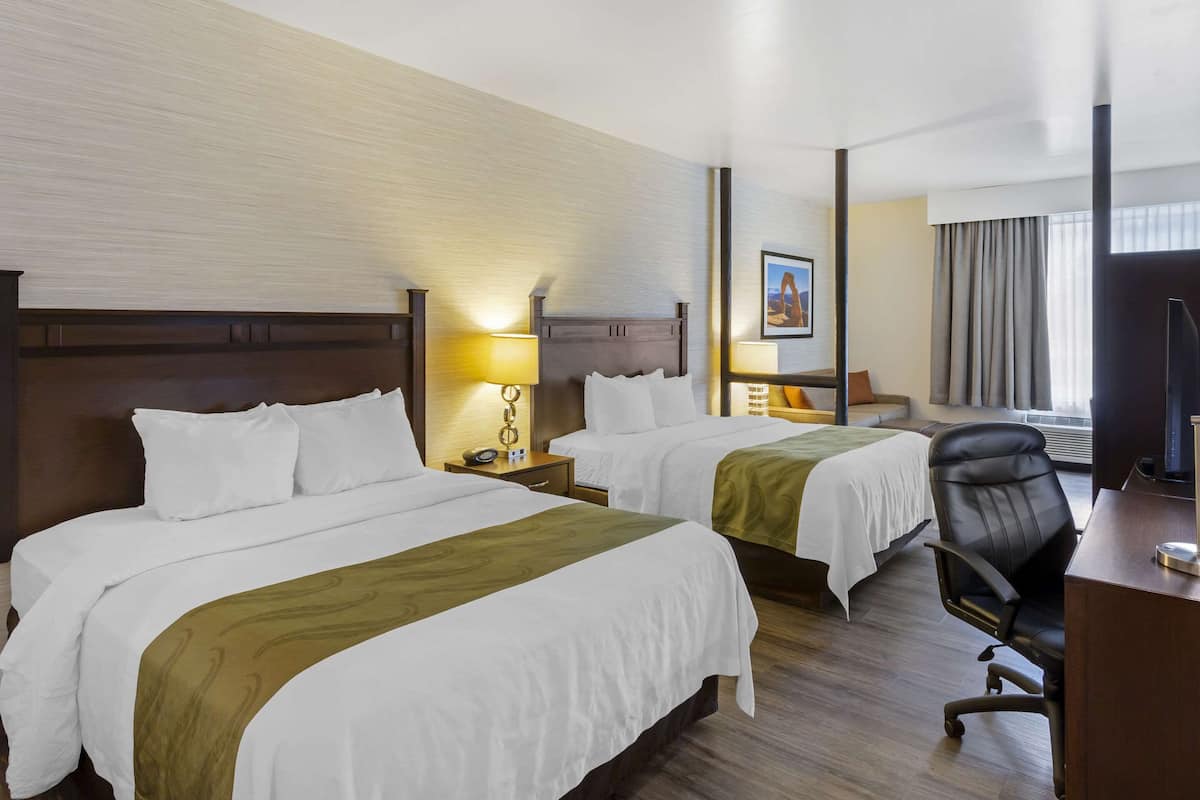 Habitación de hotel con dos camas, un escritorio, una silla y un televisor.