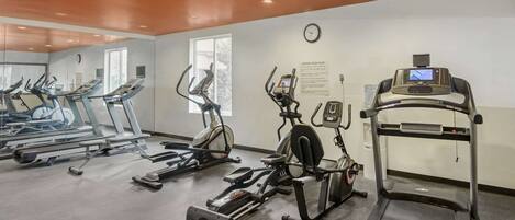 Une salle de sport équipée de tapis de course, de vélos elliptiques et d’un appareil d’aviron.