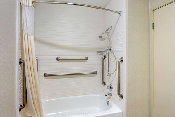 Un baño con una bañera blanca, barras de apoyo y cabezal de ducha.
