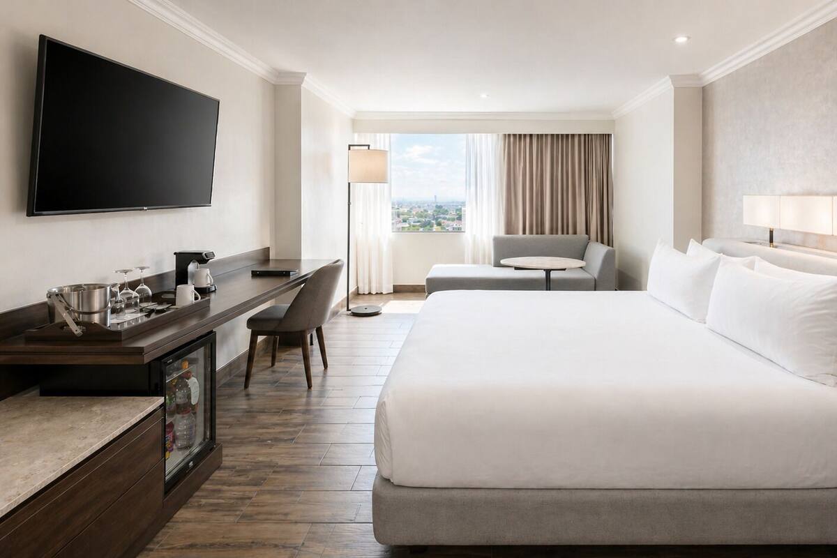 Habitación de hotel con cama, escritorio con cafetera, televisor y vista de la ciudad.