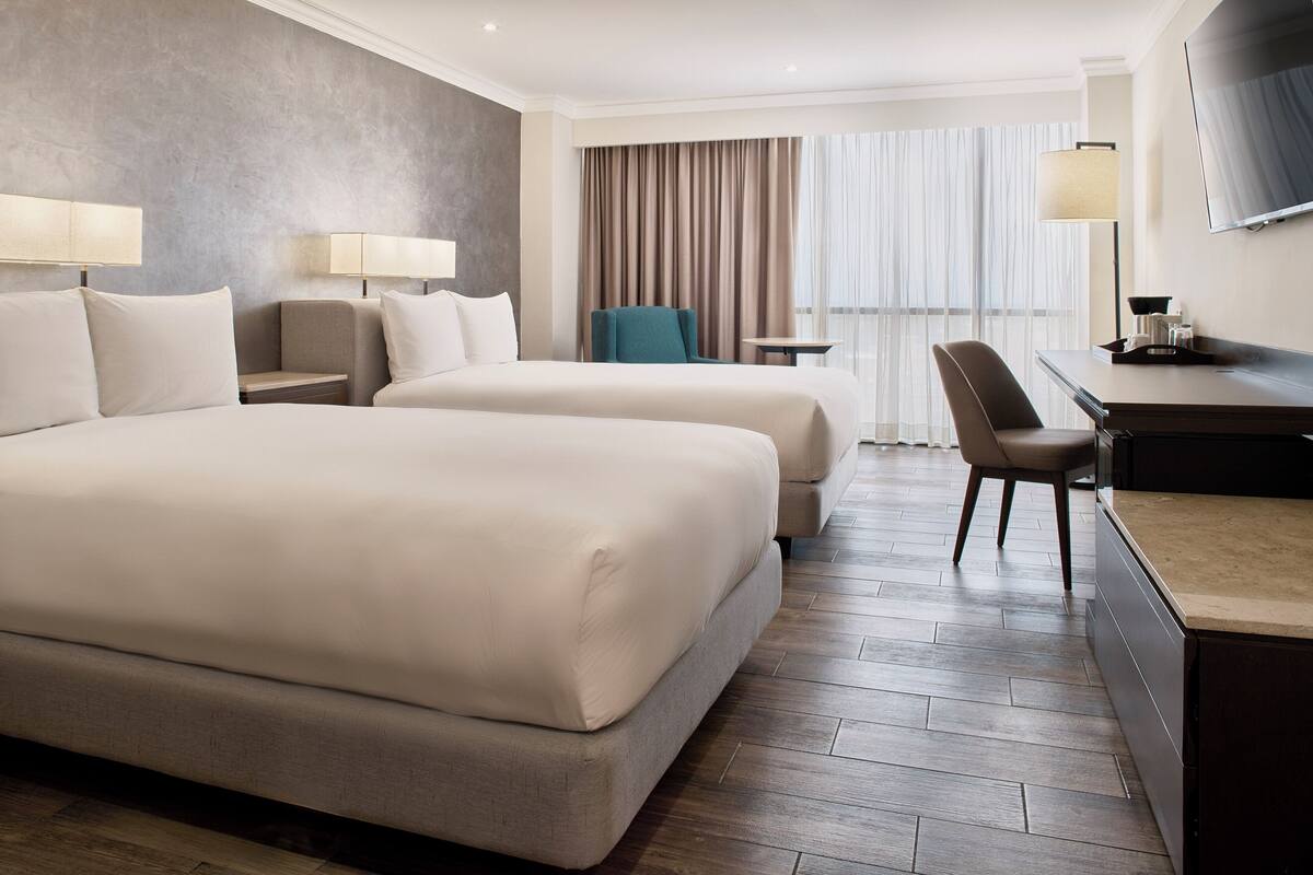 Habitación de hotel con dos camas, un escritorio, una silla, un televisor y una ventana con cortinas.