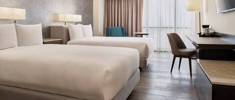 A hotel room with two beds, a desk, a chair, a TV, and a window with curtains.