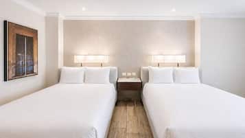 Una habitación de hotel con dos camas, una mesita de noche y una lámpara de pared.