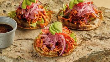 Tres tacos sobre una superficie de piedra con un tazón pequeño de salsa.