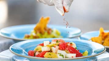 A person in a white glove seasoning a dish on a blue plate.