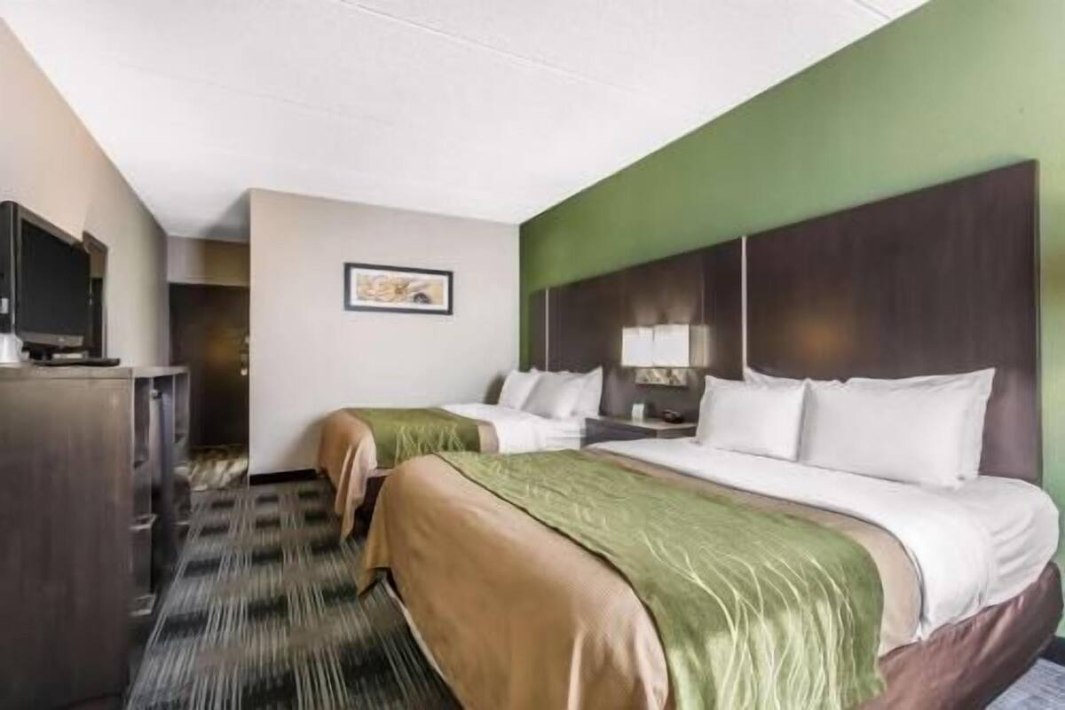 A hotel room with two beds, a desk, a television, and a framed picture on the wall.