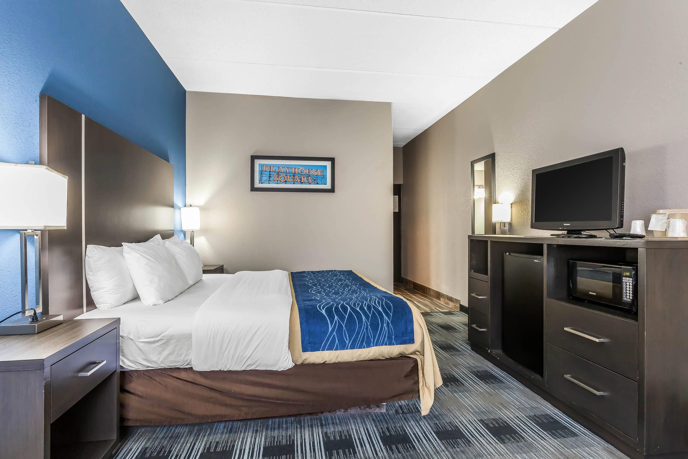 A hotel room with a bed, a desk, a television, a microwave, and a framed sign on the wall.