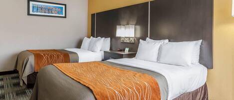 A hotel room with two beds, a headboard with a mirror, a framed picture on the wall, and a nightstand with a lamp.