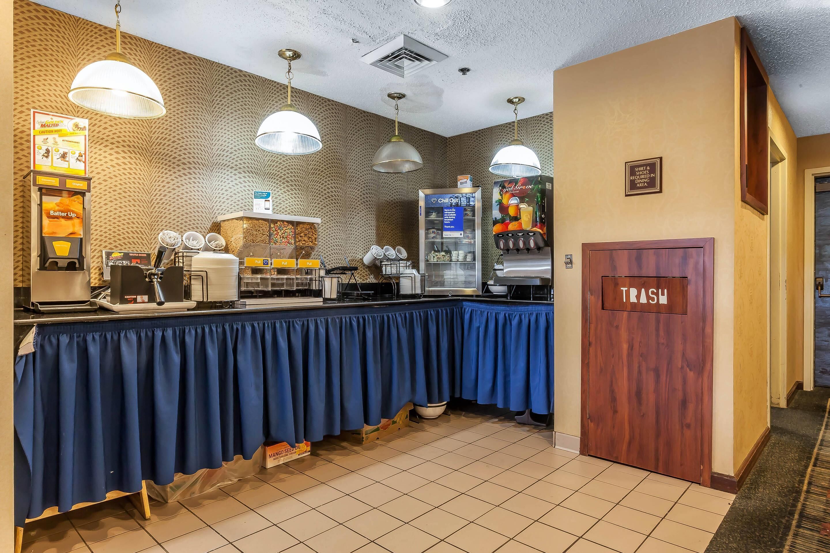 A buffet setup with a blue-covered counter, a trash bin, and a refrigerator with a beverage dispenser.