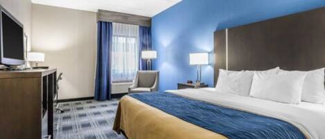 A hotel room with a large bed, a desk with a TV, a chair, and a window with curtains.