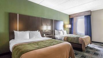 Quarto de hotel com duas camas, mesa de cabeceira com abajur e janela com cortinas.