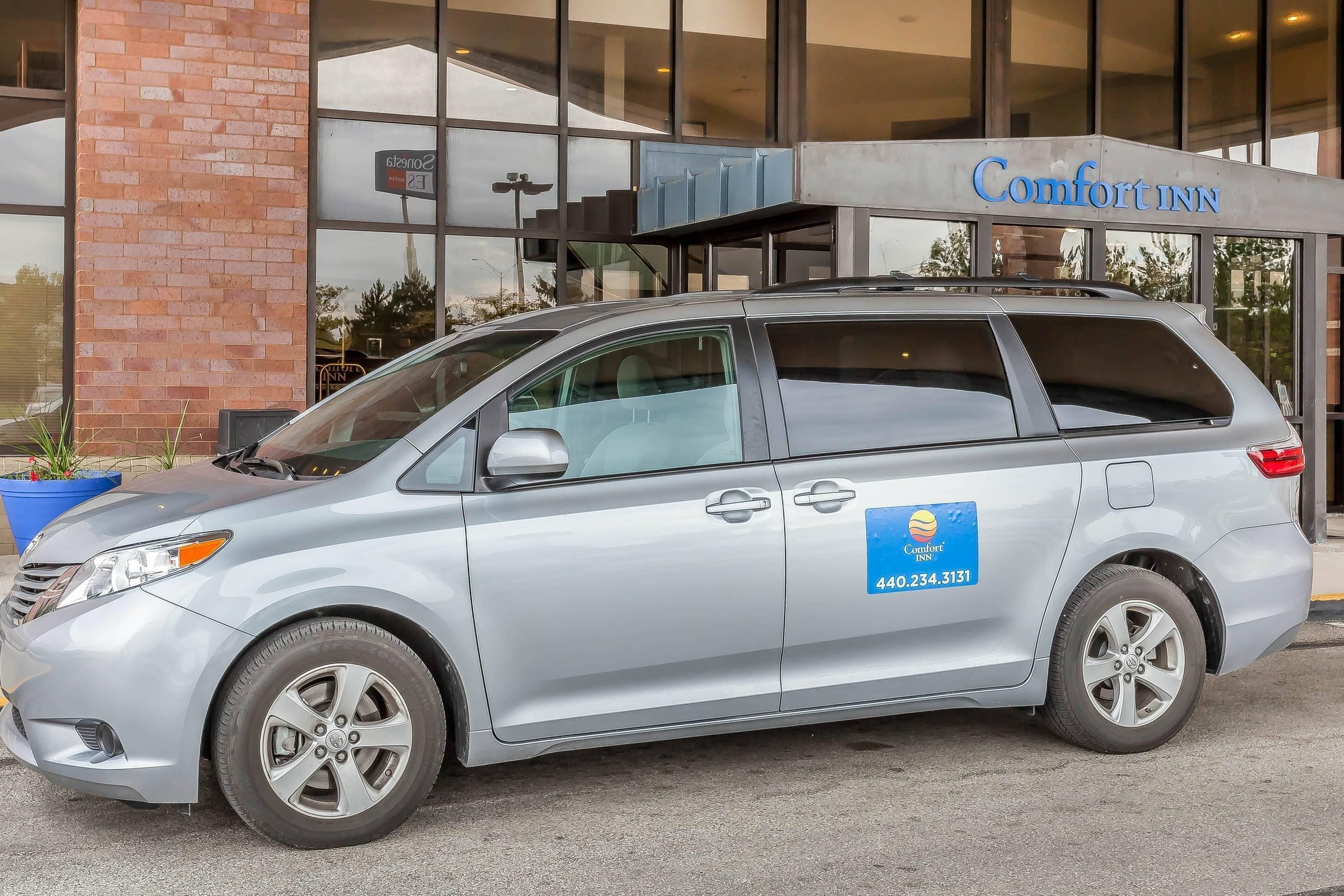 Ein silberner Minivan parkt vor einem Comfort Inn Hotel, mit einer gut sichtbaren Telefonnummer an der Seite.