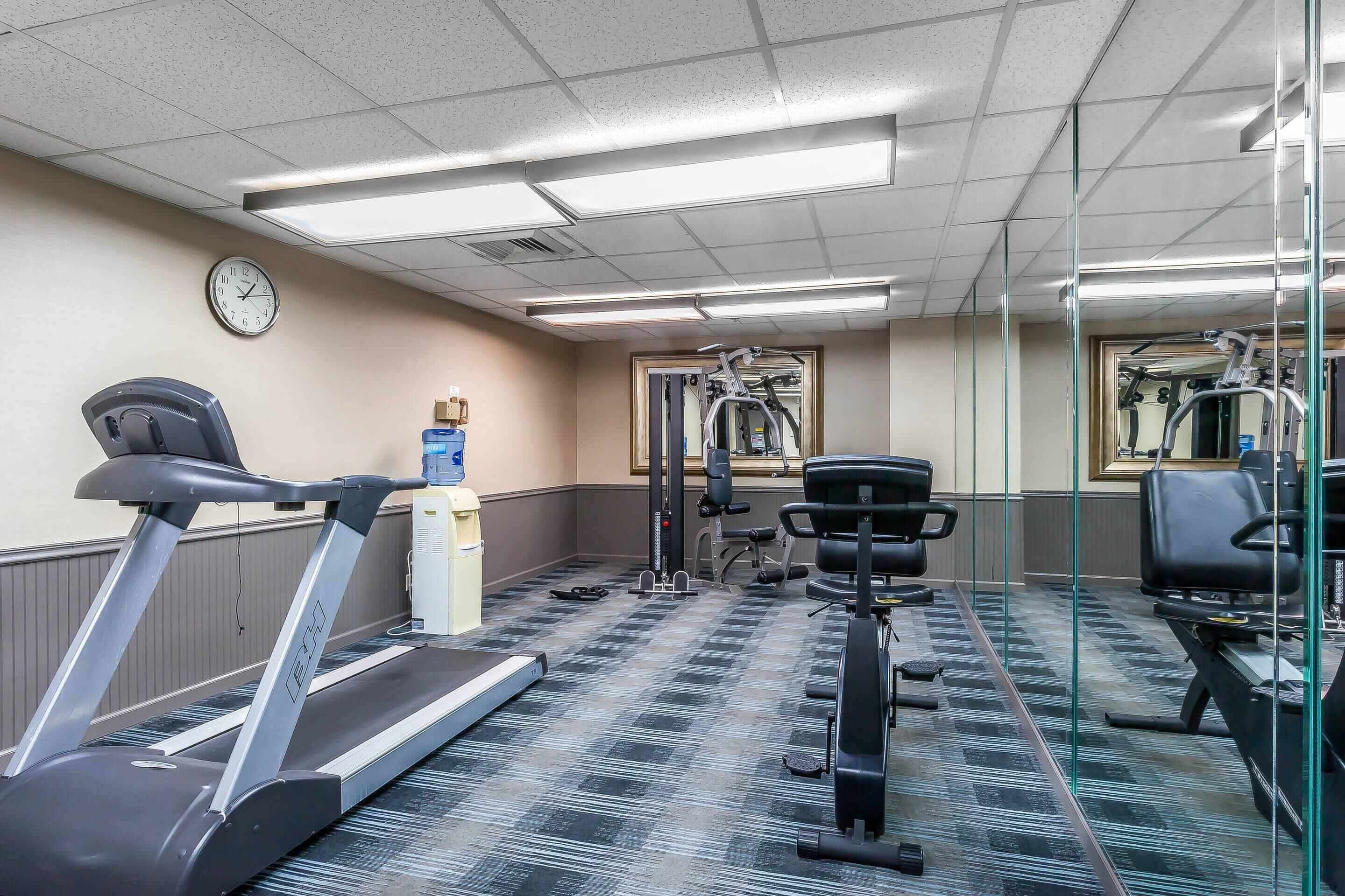 Une salle de sport équipée de tapis de course, d’appareils d’exercice, d’une horloge et d’un distributeur d’eau.