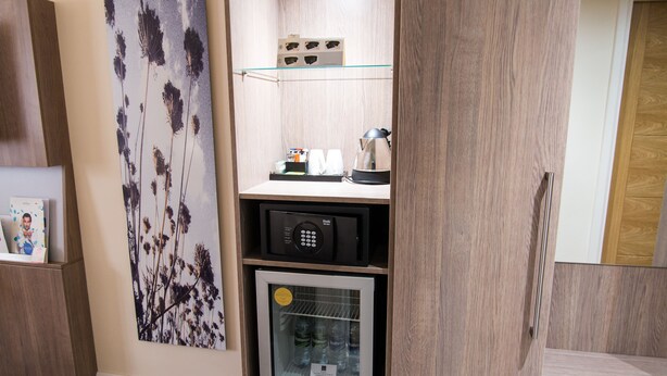 A compact kitchenette with a microwave, a small refrigerator, and a glass shelf above. - Novotel Coventry M6/J3 (Coventry)