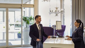 A hotel reception area with a modern design, featuring a reception desk, a chandelier, and large windows. - Novotel Coventry M6/J3 (Coventry)