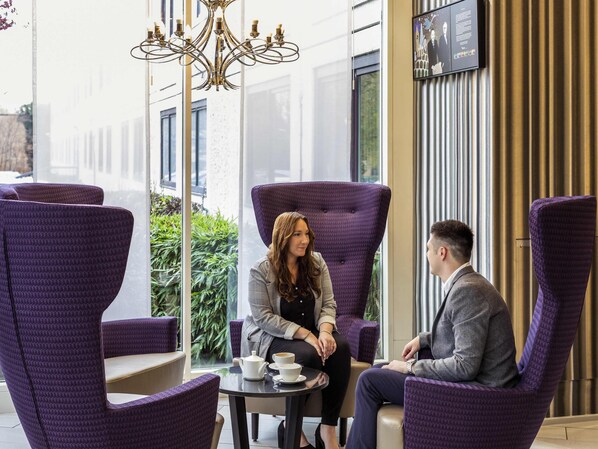 A modern indoor seating area with purple upholstered chairs and a chandelier.