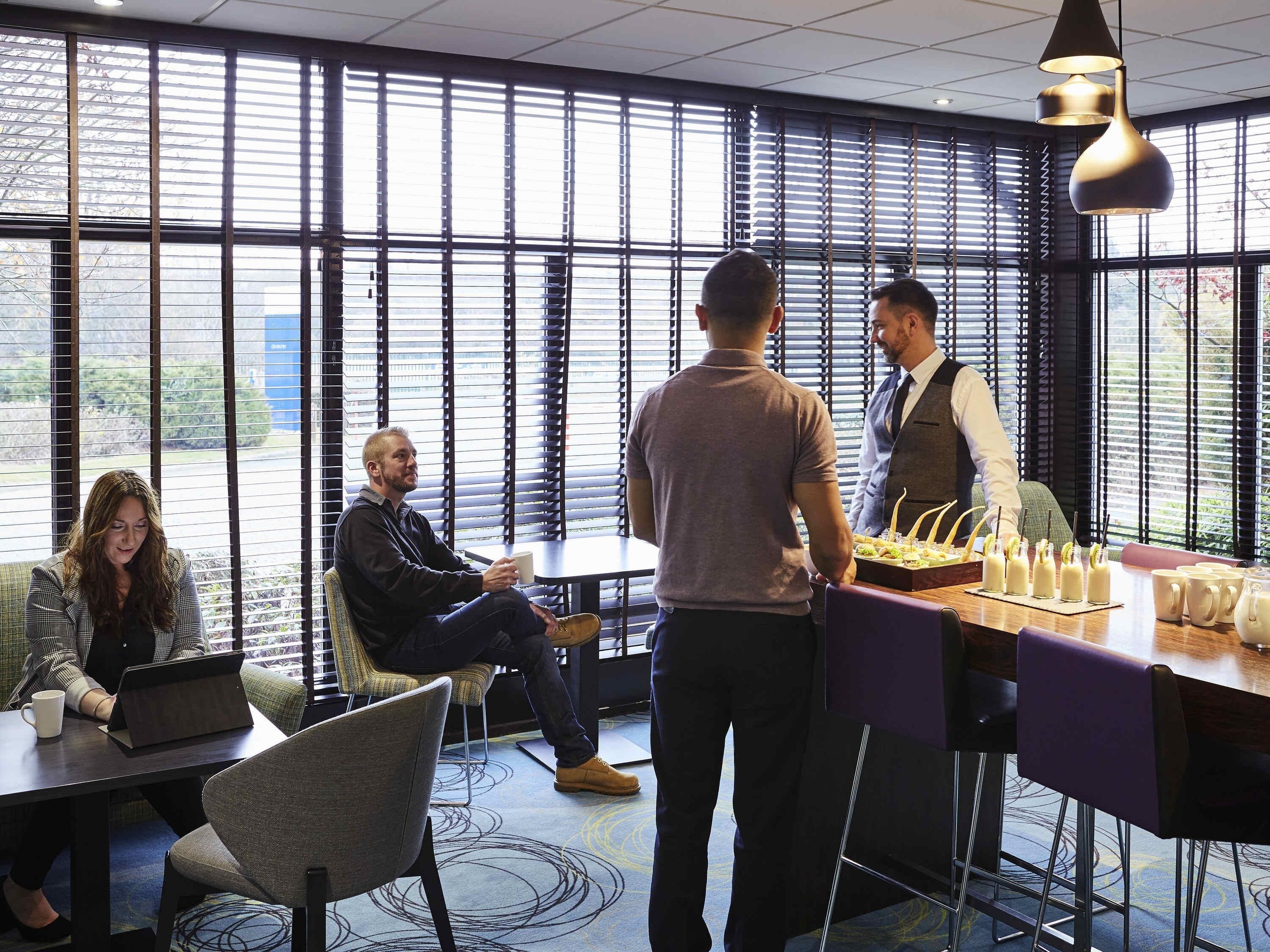 Ein moderner Büroraum mit großen Fenstern, einem Konferenztisch und einer Bar mit Getränken.
