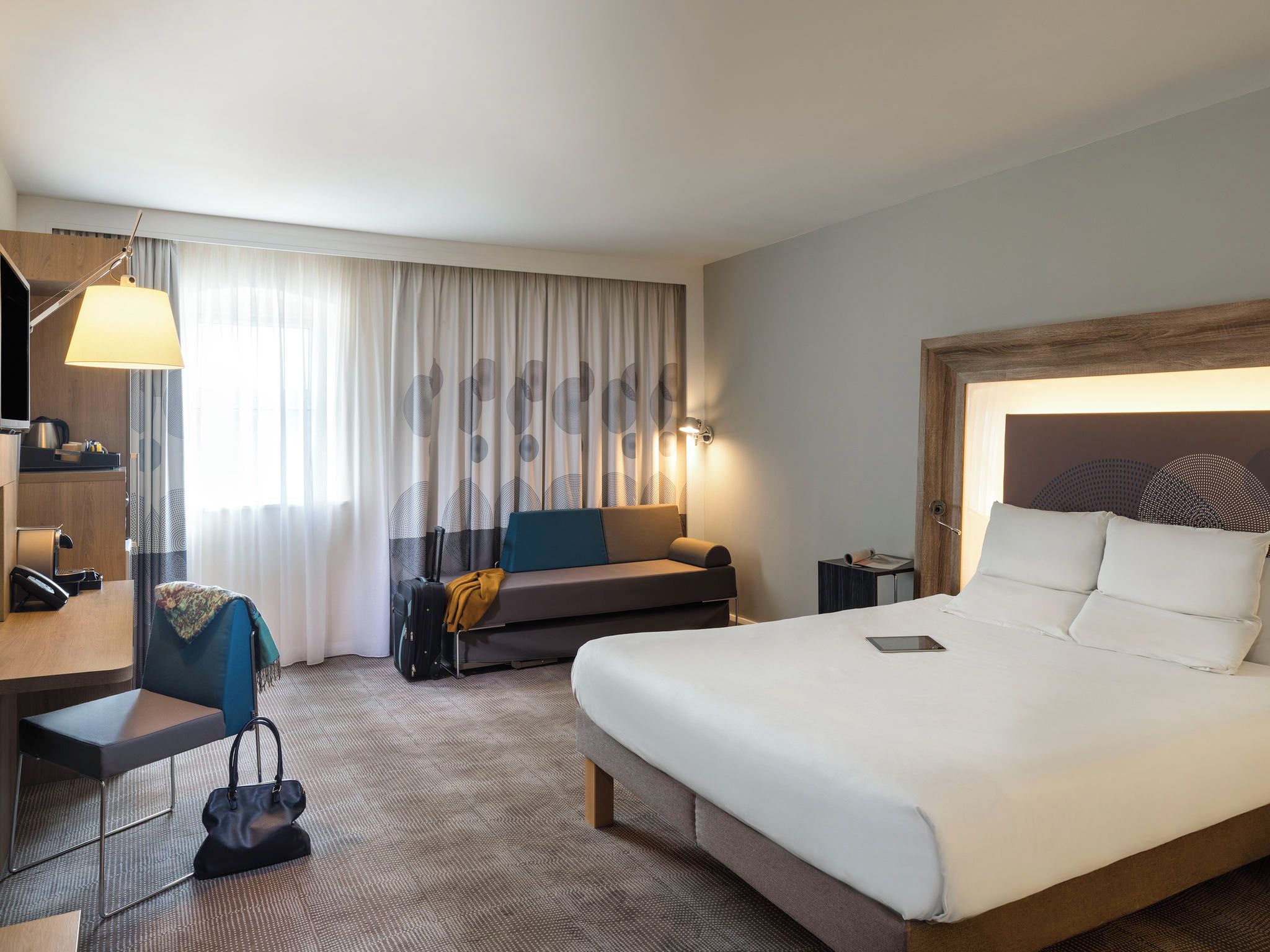 Une chambre d’hôtel avec un lit, un bureau, une chaise, un canapé et une lampe.