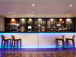 A bar area with a long counter, bar stools, and shelves stocked with bottles.