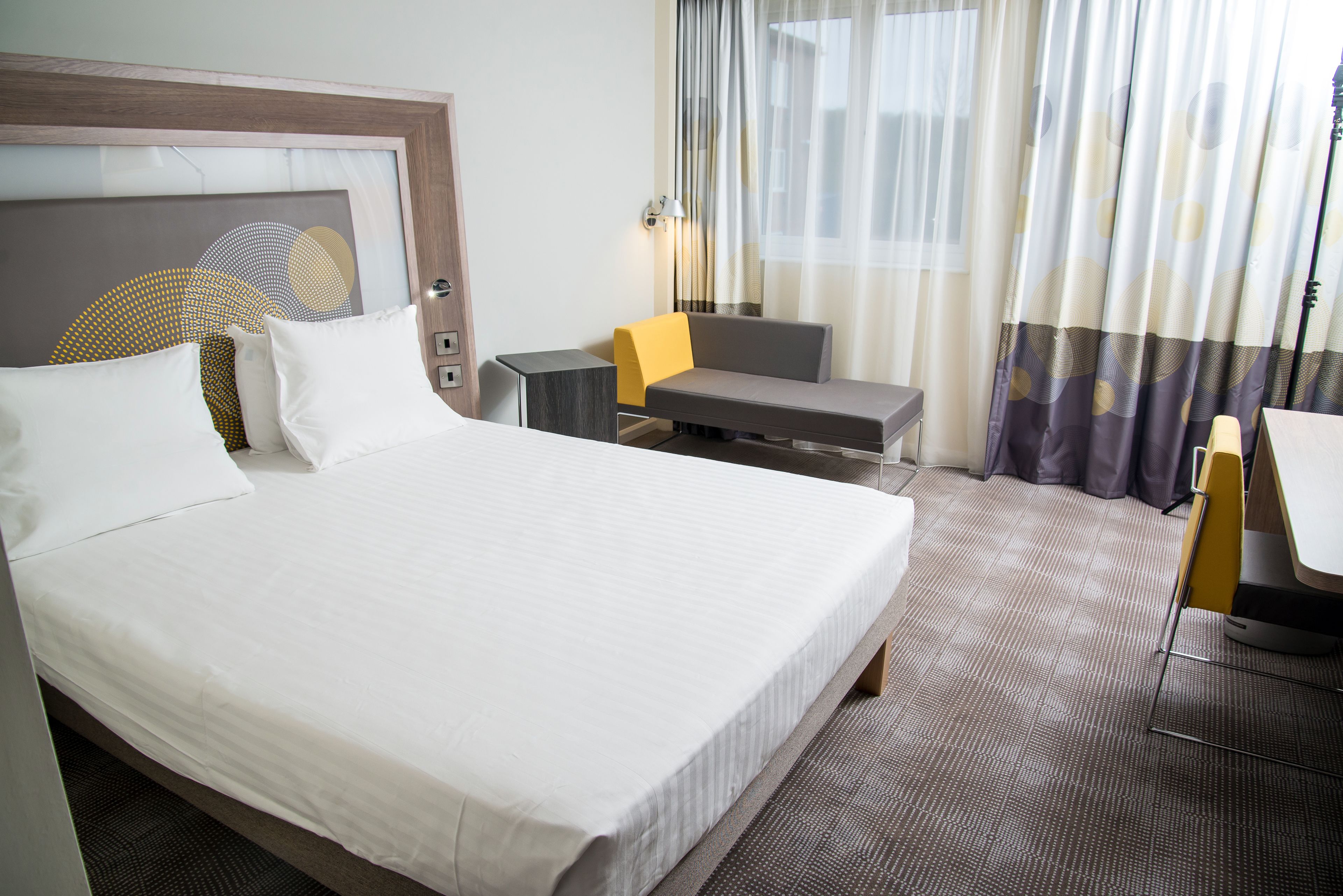 A hotel room with a large bed, a desk, a chair, and a small table.