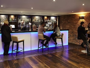 A bar area with a counter, stools, and a brick wall. - Novotel Coventry M6/J3 (Coventry)