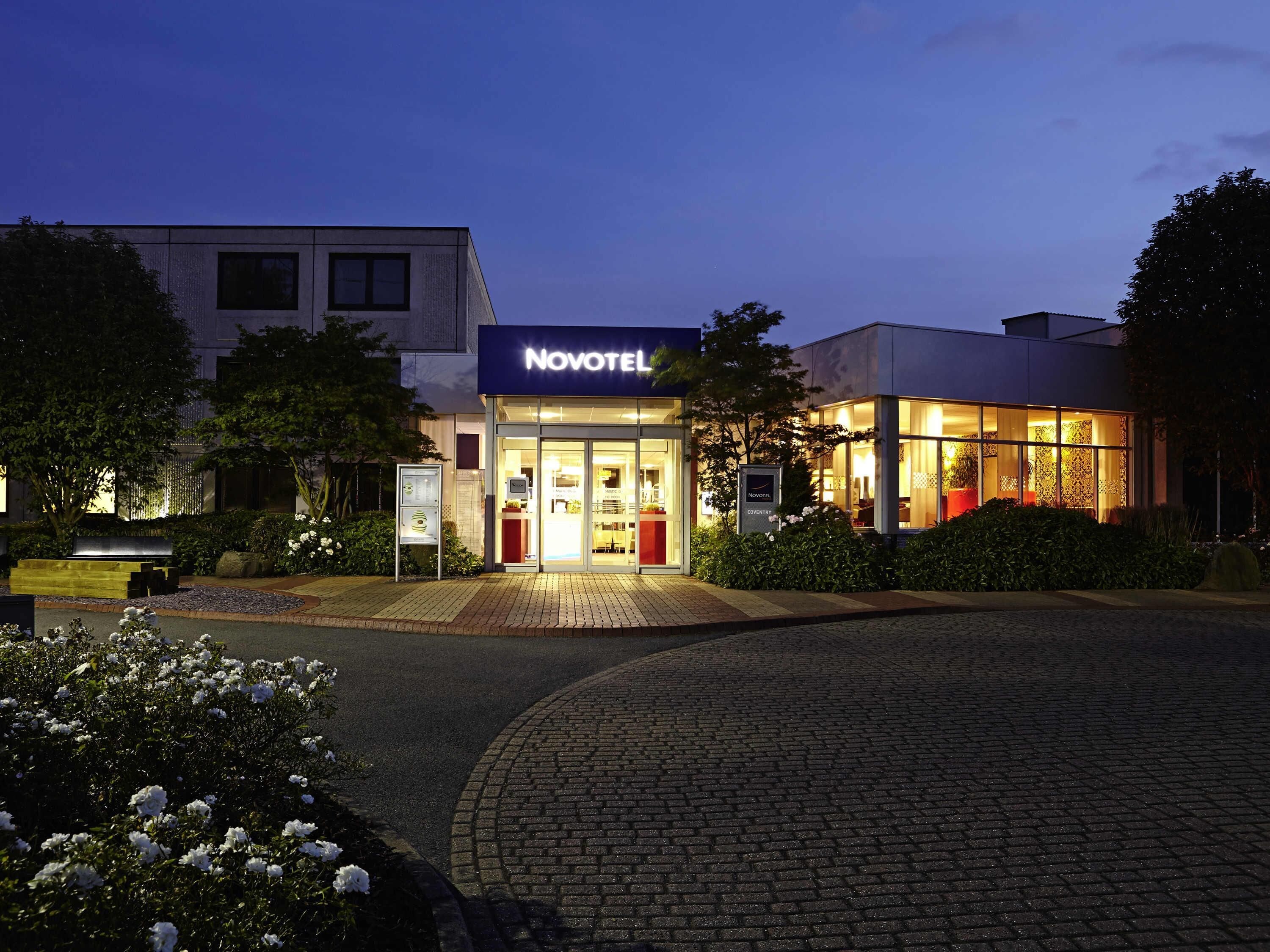 A hotel with a modern facade, a well-lit entrance, and a paved driveway.