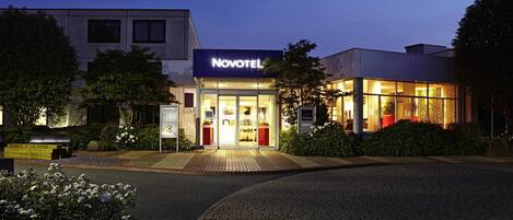 A hotel with a modern facade, a well-lit entrance, and a paved driveway.