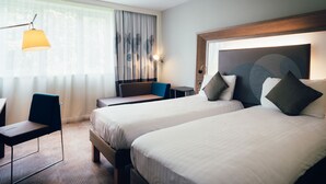 A hotel room with two beds, a desk, a chair, and a lamp. - Novotel Coventry M6/J3 (Coventry)