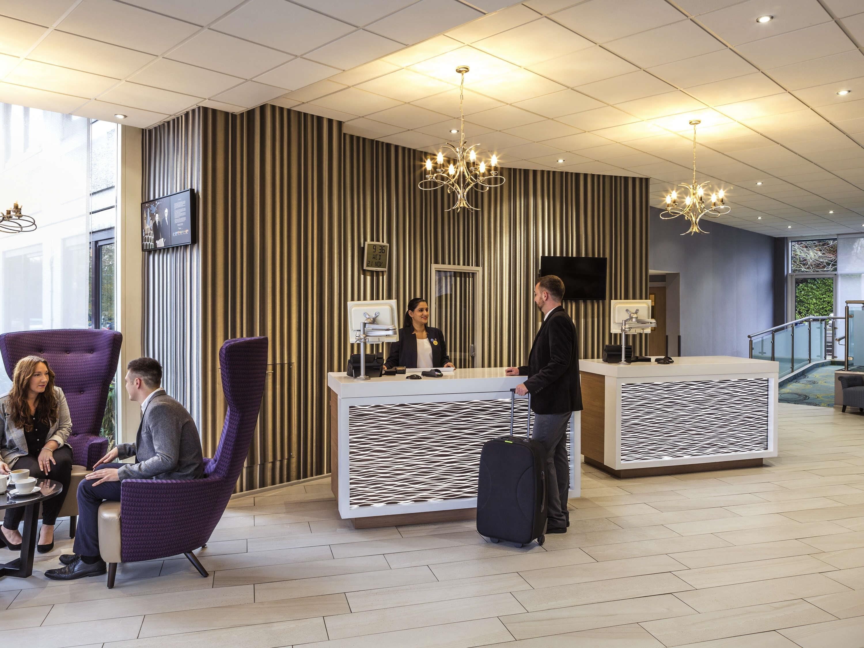A hotel lobby with a reception desk, seating area, and a staircase.