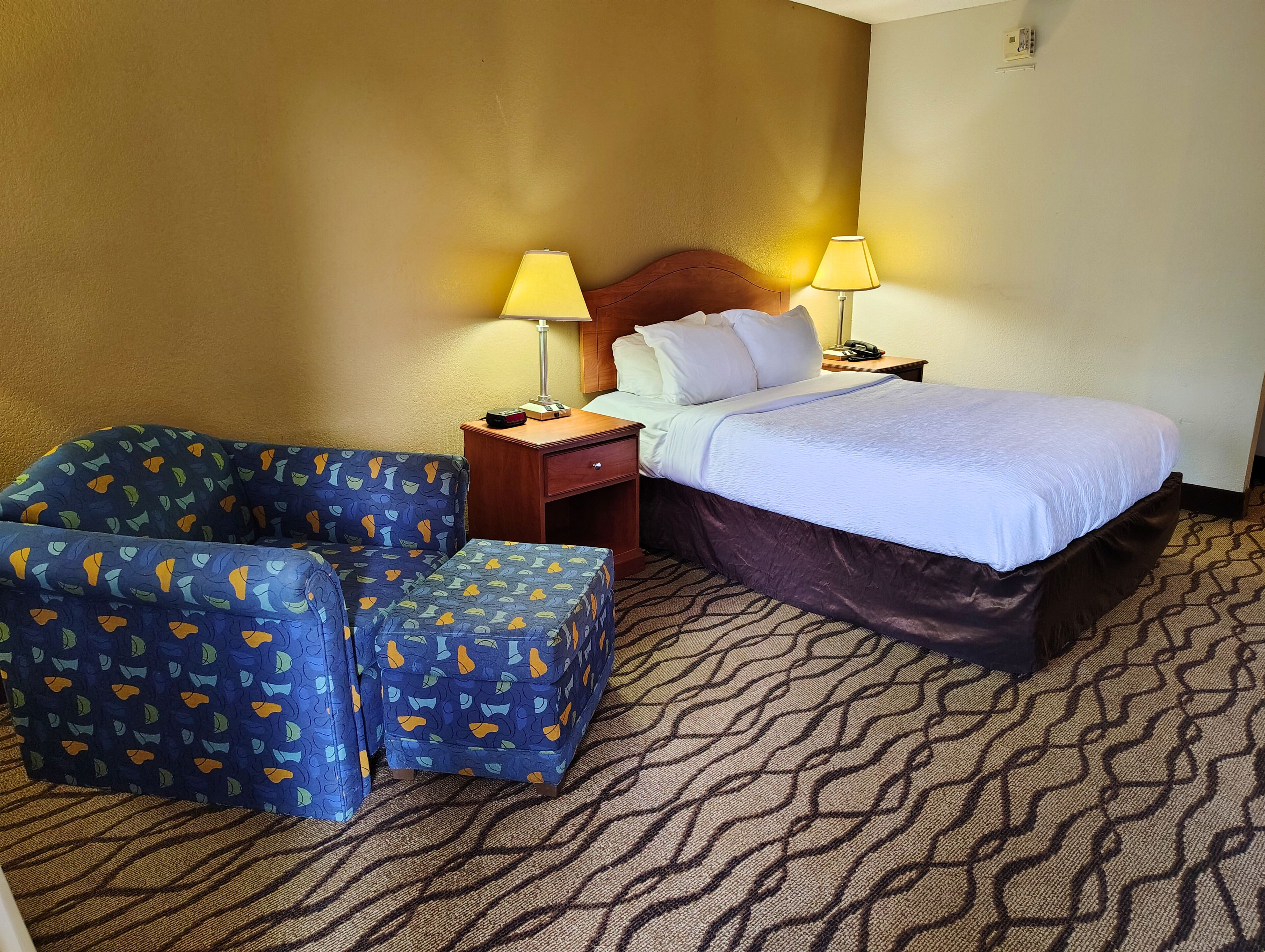 A hotel room with a bed, two bedside tables with lamps, a chair, and a patterned carpet.
